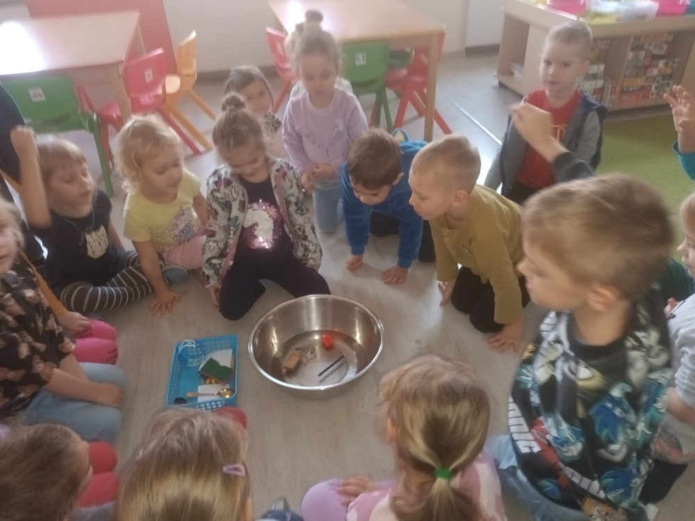 Co pływa, co tonie? - zdjęcie 2 - dzieci siedzą w kole i kolejno wrzucają przedmioty do wody obserwując czy zatoną.