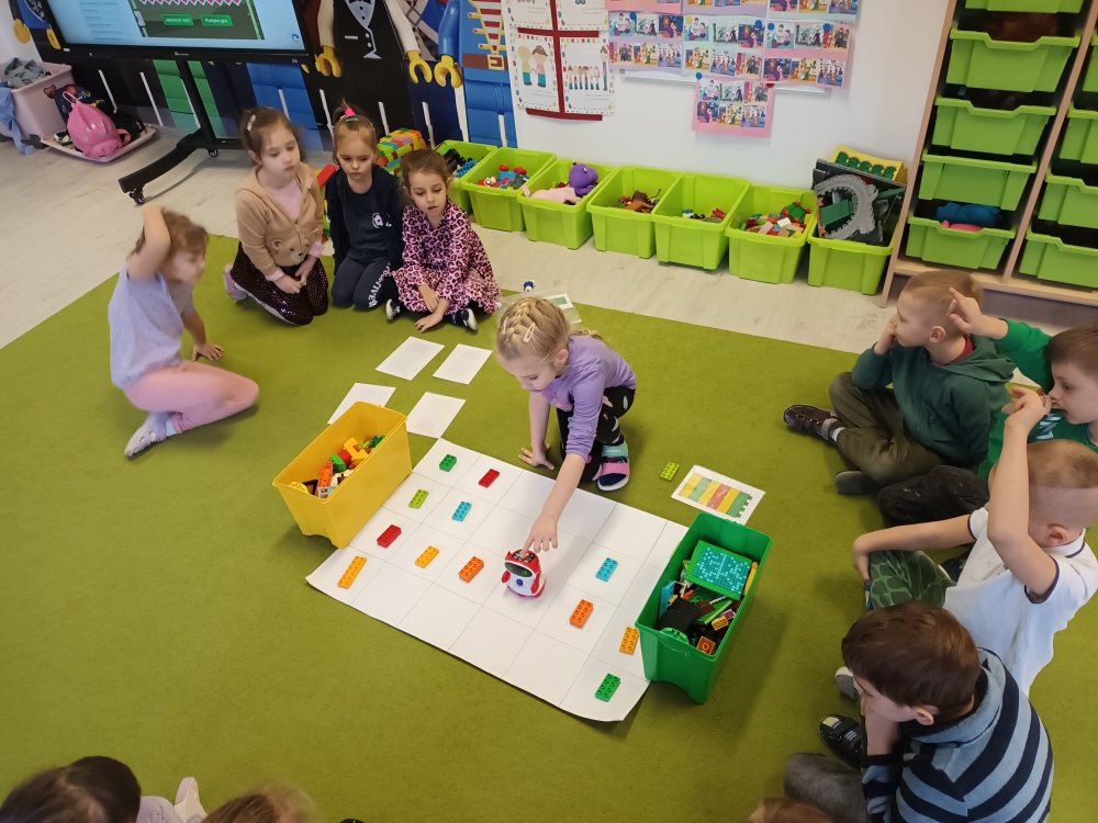 Dzień Lego - dzieci siedzą na dywanie i uczestniczą w zabawie z wykorzystaniem klocków Lego i robota Doc 