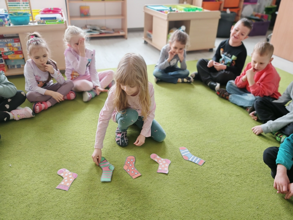 Dzień kolorowej skarpetki - Maja zmienia układ ułożonych na dywanie skarpetek, przygotowując zagadkę dla kolegi.