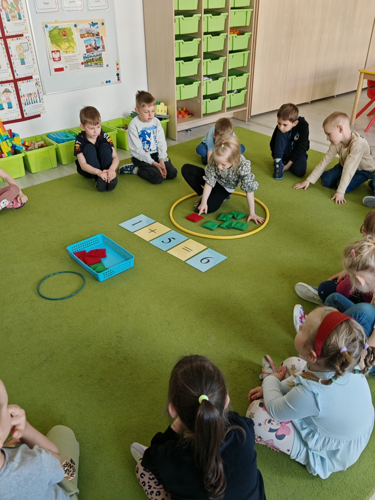 Projekt Działaj i licz - dziewczynka przeczytała działanie matematyczne, wrzuciła odpowiednią liczbę woreczków do koła, przelicza woreczki sprawdzając poprawność wykonanego zadania.